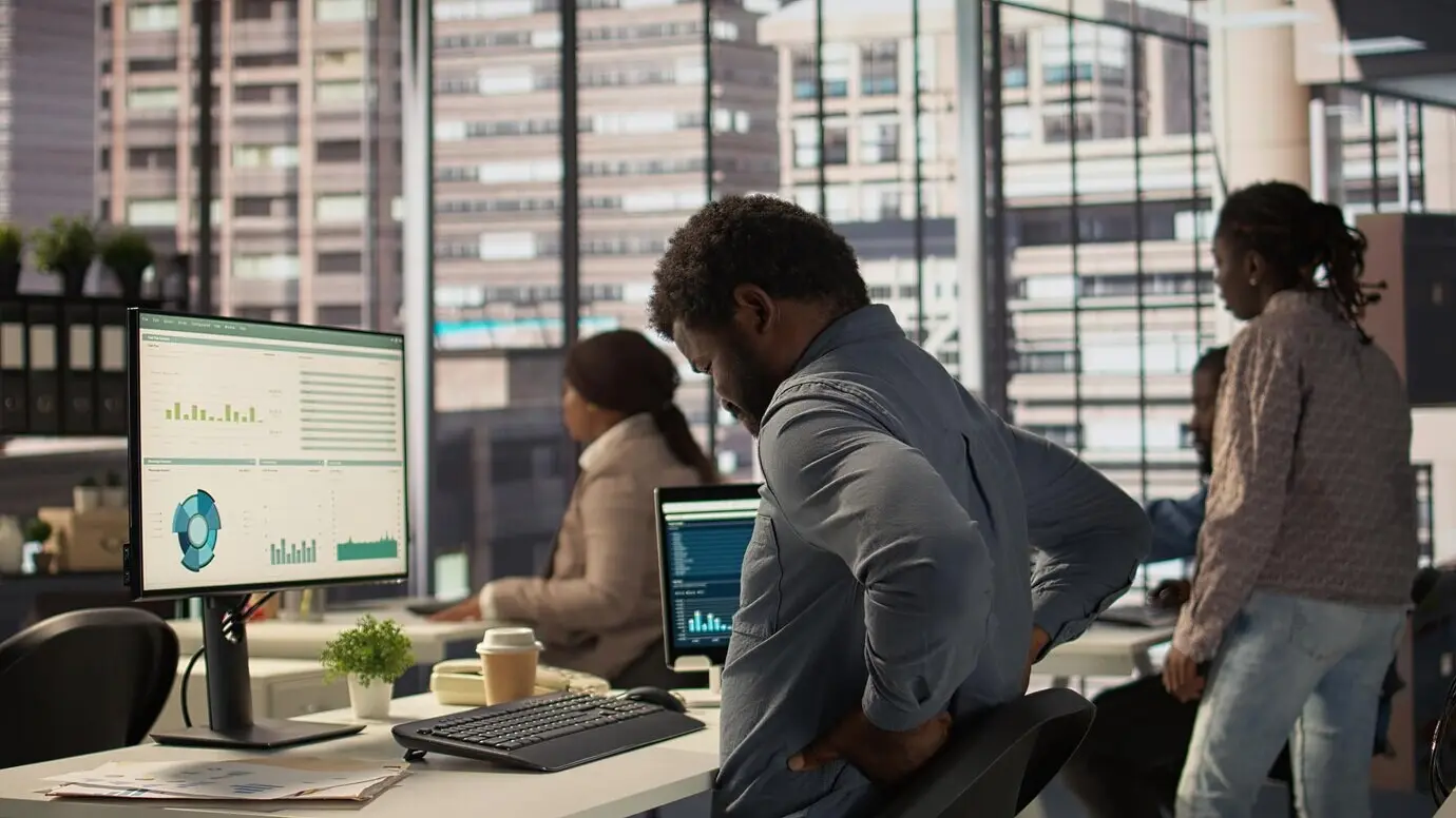 Афроамериканский сотрудник компании делает перерыв, чтобы размять спину в офисе.